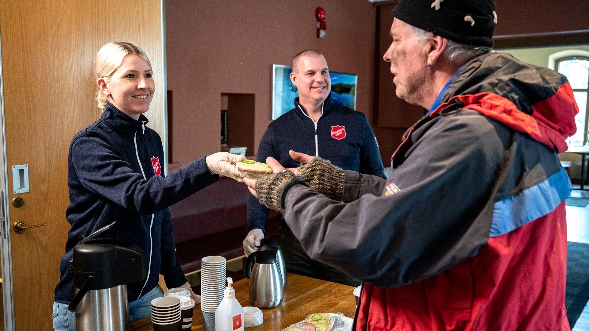 Två personer från Frälsningsarmén som delar ut en smörgås till en man i utsatthet.