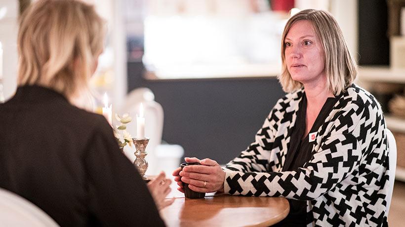 Helena Andersson som är kårledare och ansvarig för det sociala arbetet och familjearbetet på Kår 393 i Stockholm. Hon sitter vid ett bord och samtalar med en hjälpsökande mamma. Den hjälpsökande mamman sitter med ryggtavlan mot kameran.