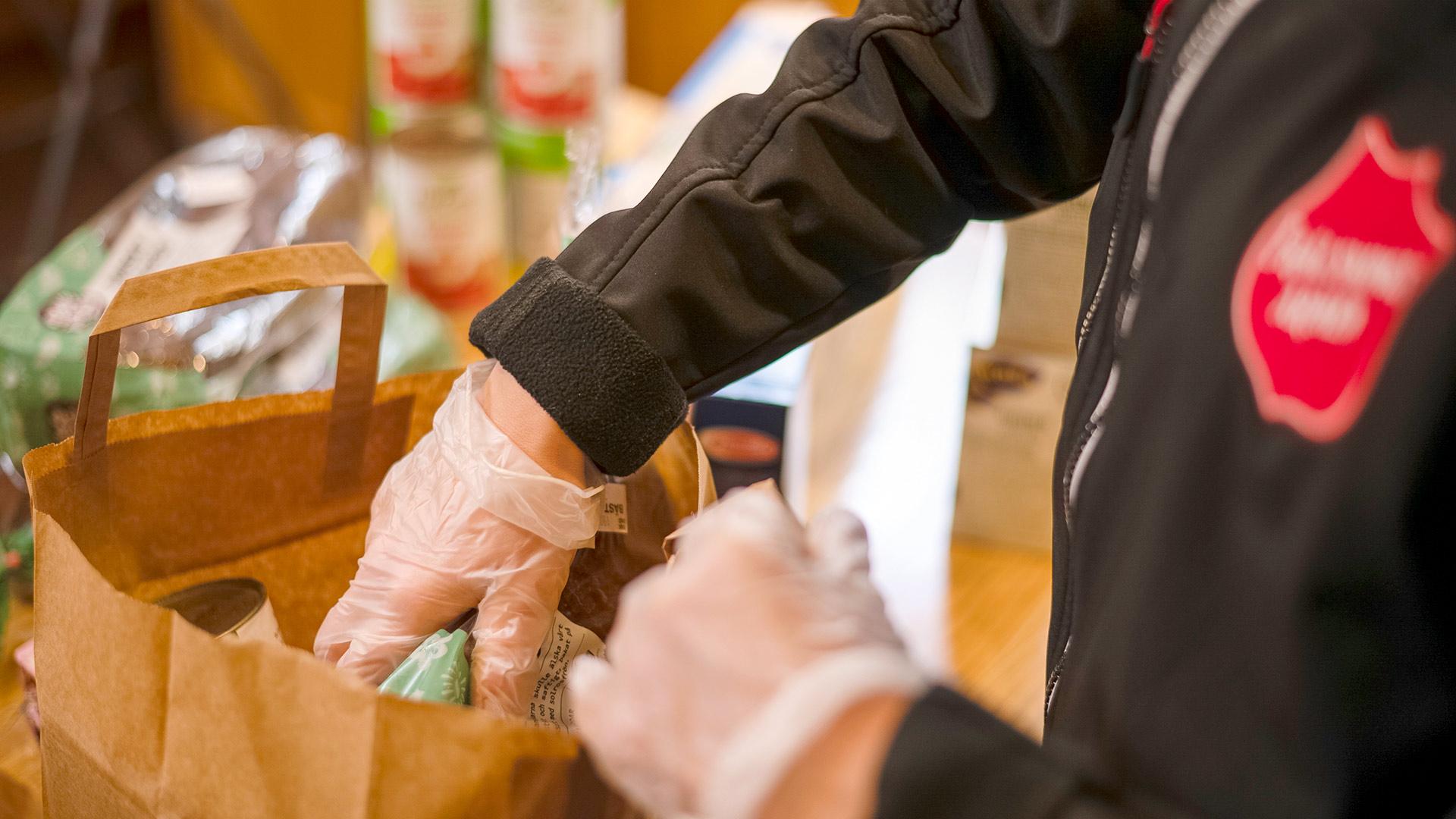 En person från Frälsningsarmén gör iordning en matkasse. I bakgrunden står det livsmedelsprodukter på bordet.