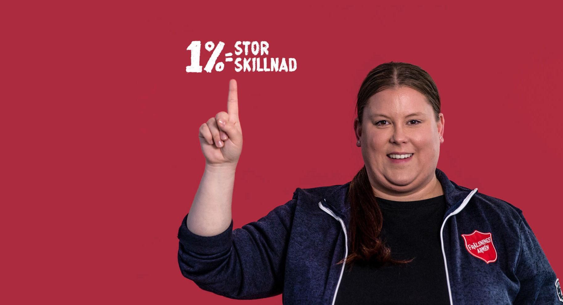 En kvinna från Frälsningsarmén som pekar upp mot en text där det står "1% = stor skillnad", och ler mot kameran.