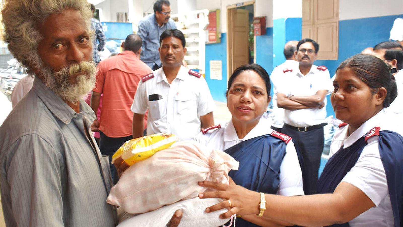En äldre man i Indien tar emot säckar med förnödenheter från två kvinnor som bär Frälsningsarméns uniform.