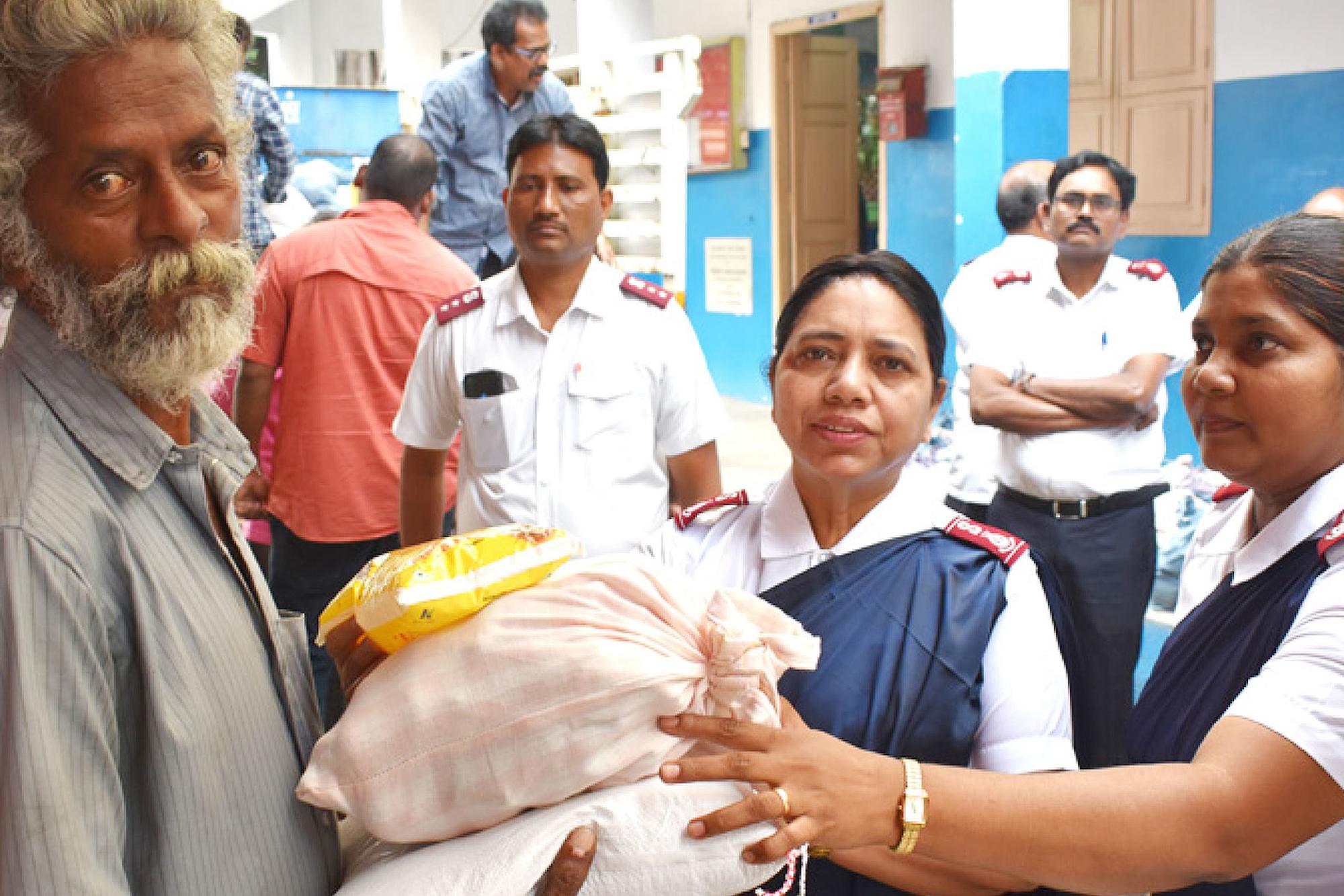 En äldre man i Indien tar emot säckar med förnödenheter från två kvinnor som bär Frälsningsarméns uniform.