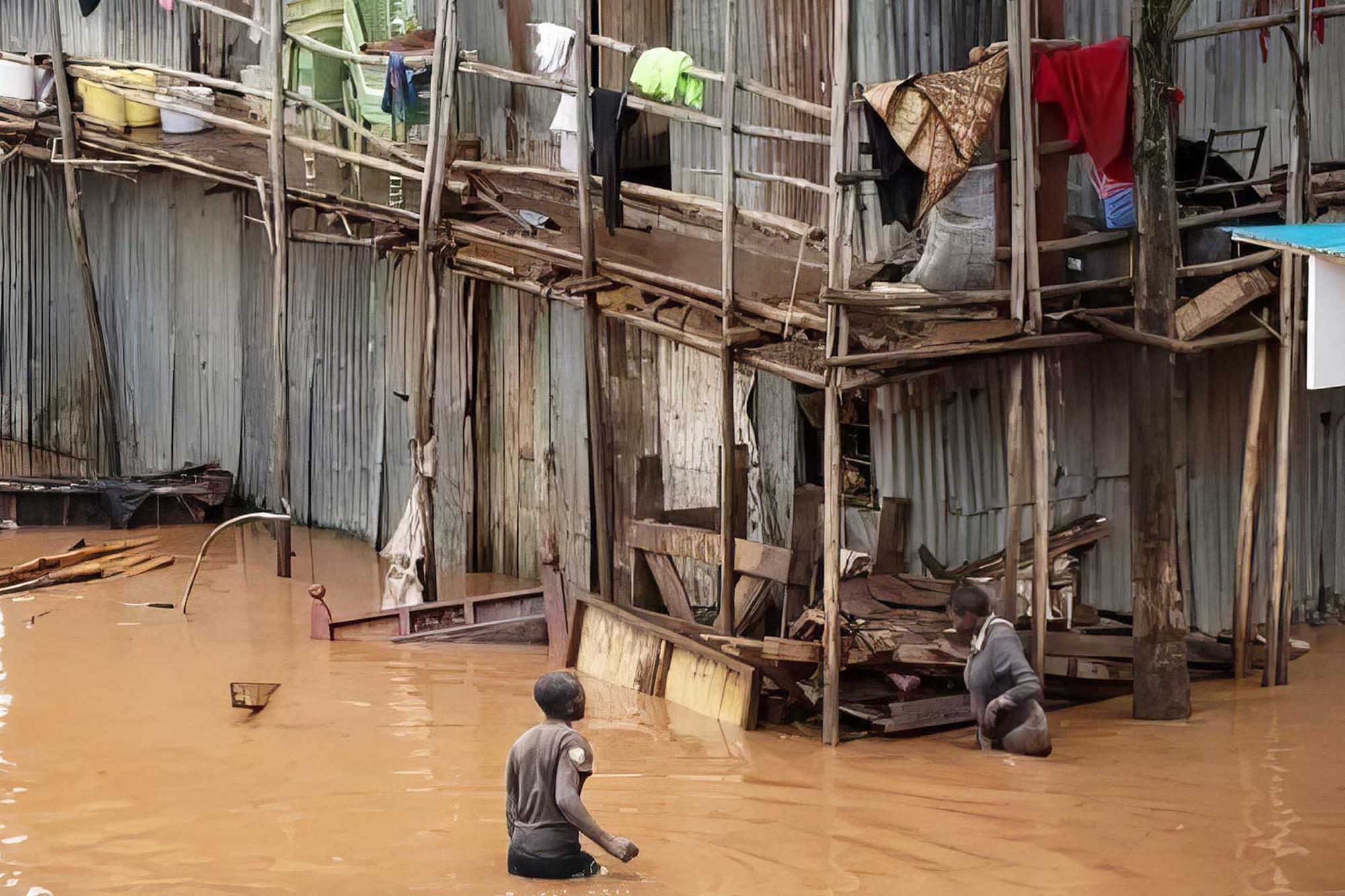 Översvämning i Kenya - två personer vadar i vatten som går upp till midjan, bakom dem syns en stor barack med en massa bråte och två våningar och loftgång. 
