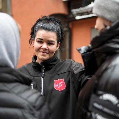 En kvinna med Frälsningsarméns sköld på jackan samtalar med två personer som har ryggen mot kameran.