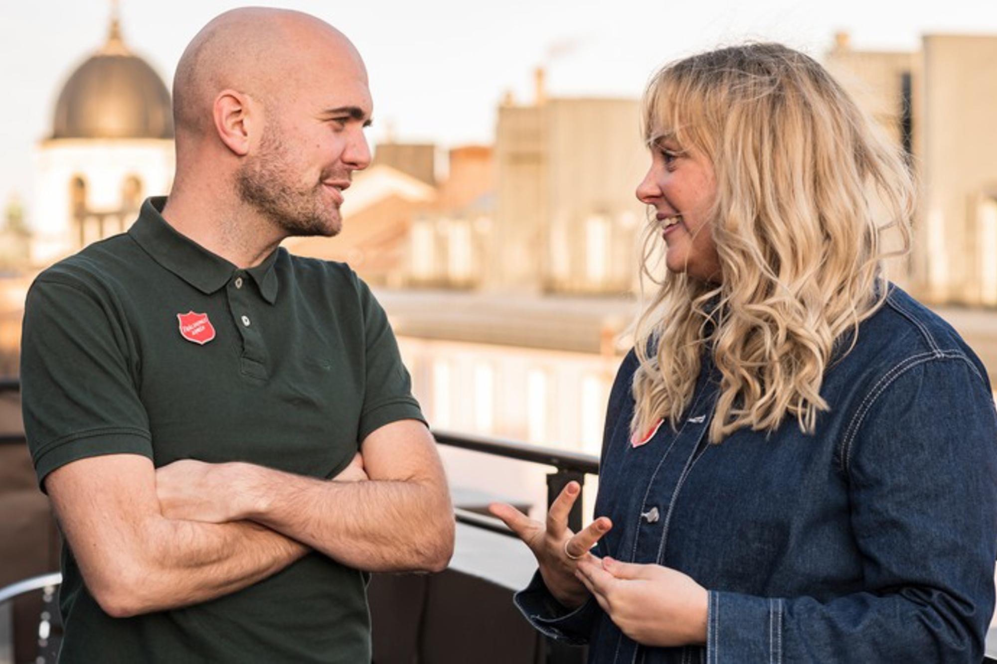 Till vänster: Christian Edlund som är samordnare för stödarbetet inom Starta Om. Till höger: Johanna Lindhult som är astor, själavårdare och projektutvecklare på Starta Om. De står och samtalar ute på en balkong och i bakgrunden syns olika byggnader.