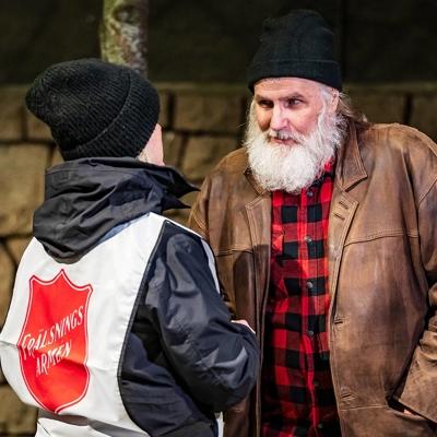 En kvinna med Frälsningsarméns sköld på ryggen samtalar med en äldre man i sliten jacka och skägg.