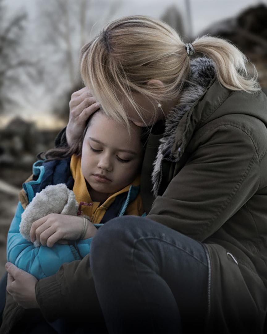 En mamma kramar om en liten flicka som ser allvarsam ut. De är utomhus och har vinterjackor på sig.